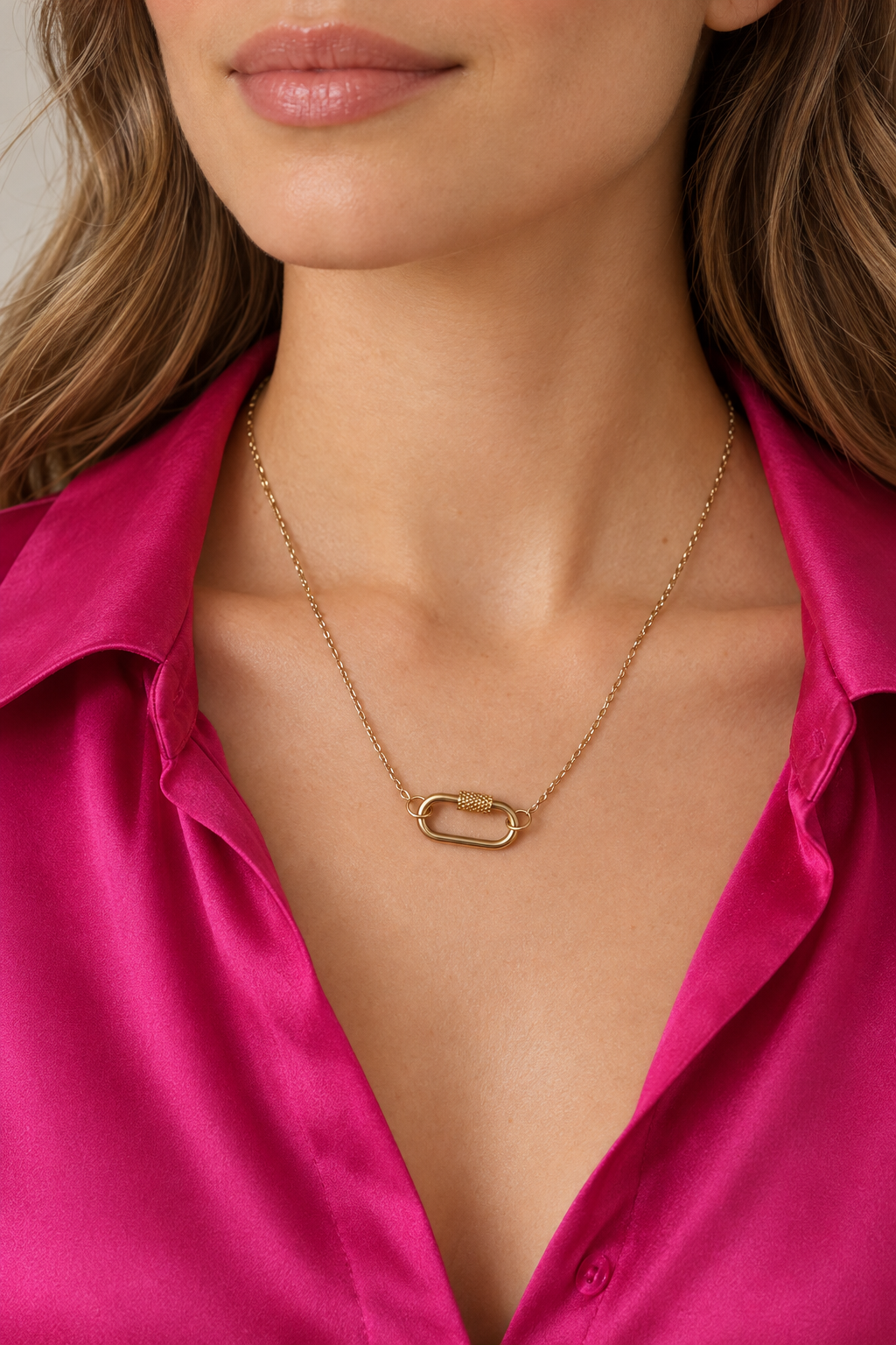Collier doré porté avec une chemise en soie fuchsia